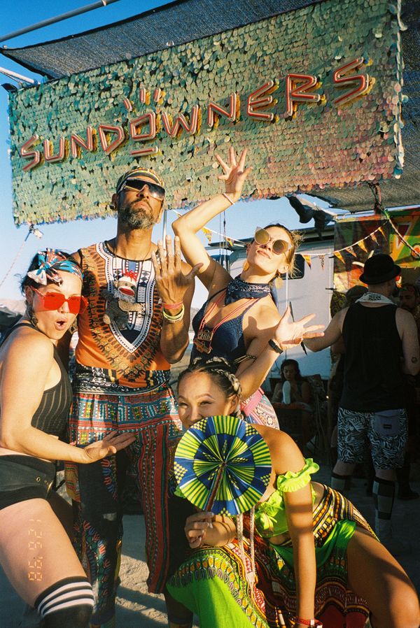 Campmates in African-print outfits posing under the sequined Sundowners sign