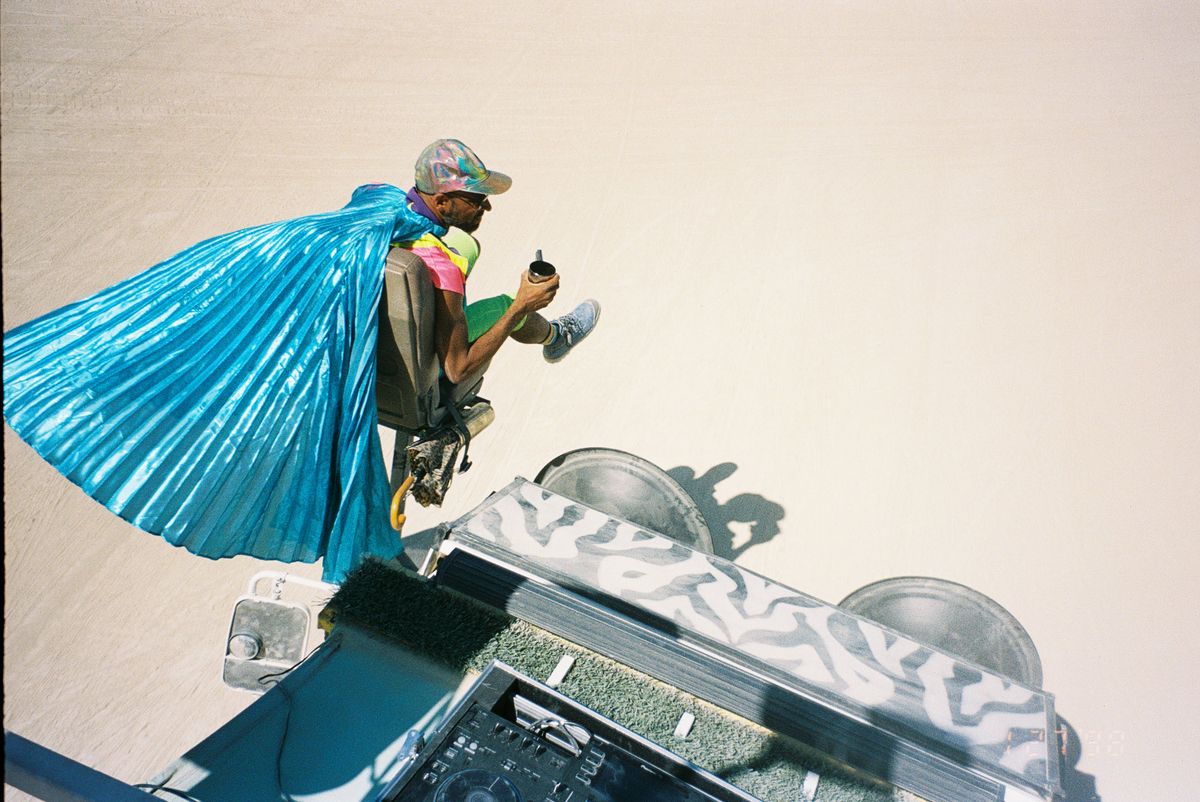 A crew member in a flowing blue cape riding Rexan’s front seat, seen from above