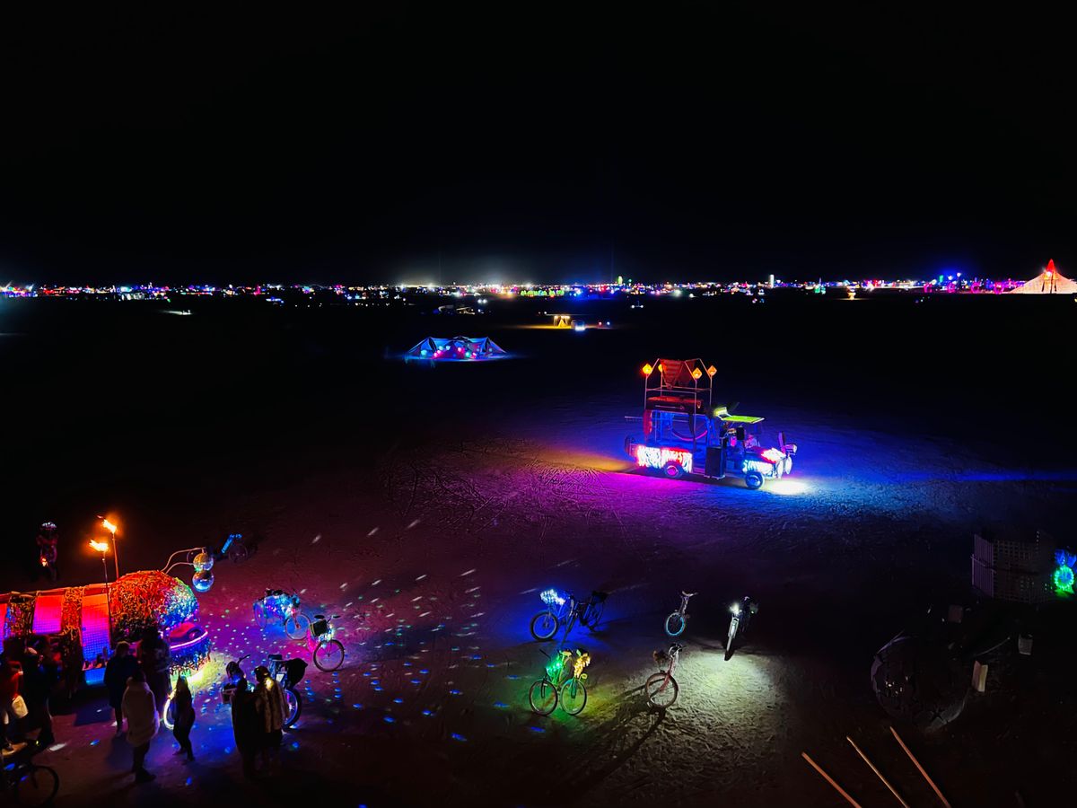 Rexan lit up on the open playa at night, with glowing bikes and art around it